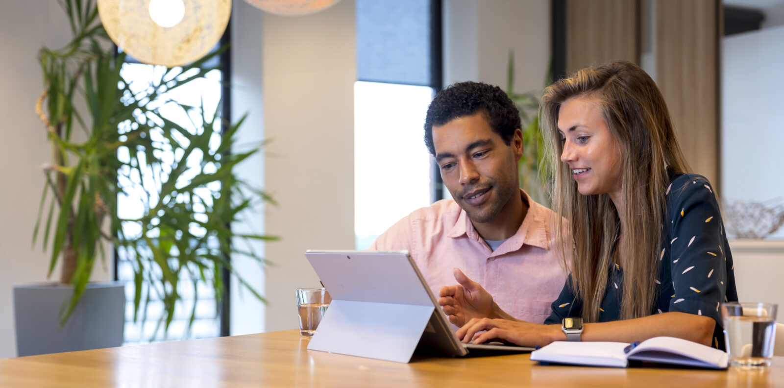 Image of two people working together on a tablet at a conference table in a bright office setting