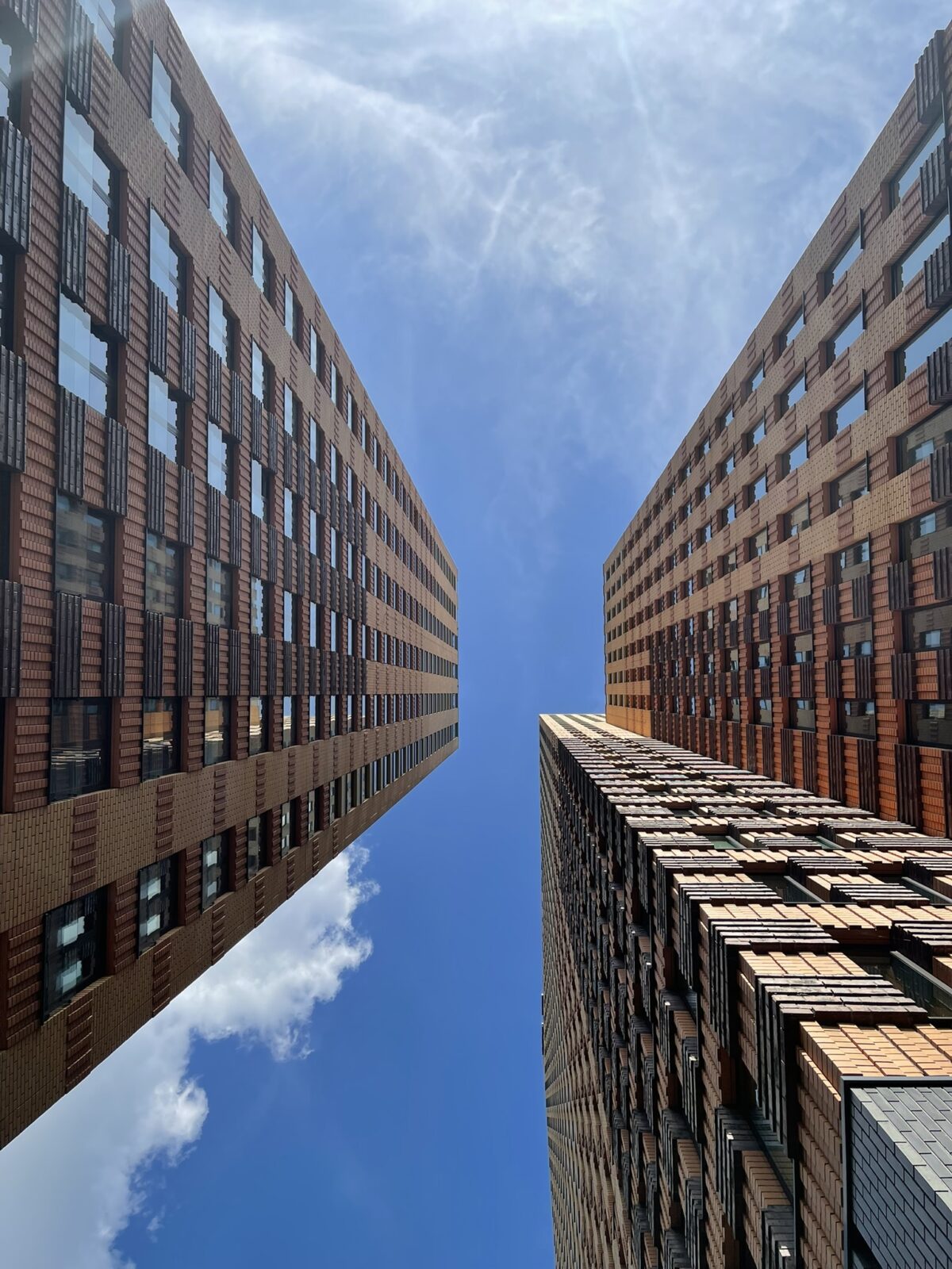 An upward view between two modern brick office buildings, with clean lines and an open blue sky