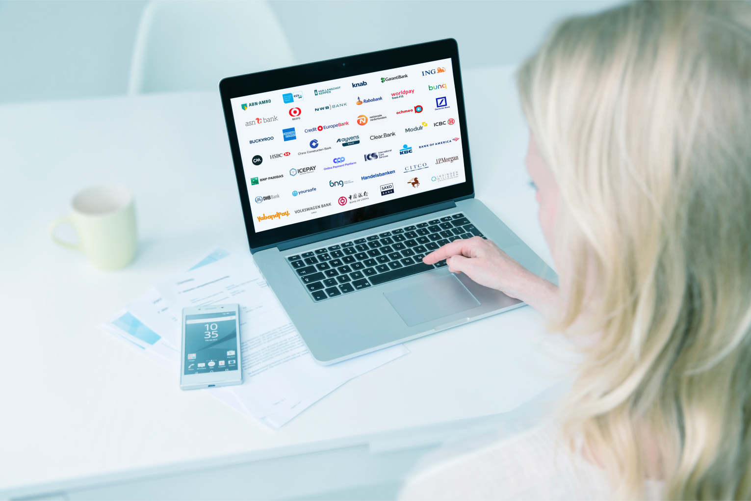 A woman looks at a laptop screen displaying the logos of members of the Dutch Payments Association