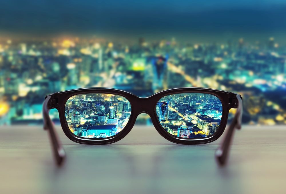 A pair of glasses on a desk, offering a clear view through the lenses of a city lit up at night