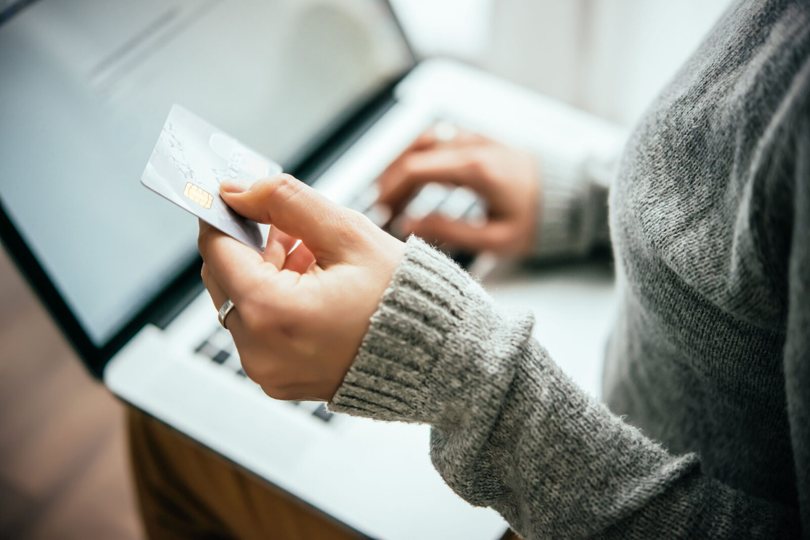 A person is holding a debit card while making an online payment on a laptop in a quiet setting