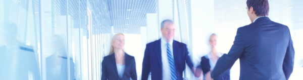A group of business professionals gathers in a bright office corridor, where two people shake hands to kick off a meeting or collaboration